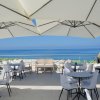 Terrazza con tavoli e sedie sotto grandi ombrelloni, vista sul mare azzurro.