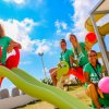 Quattro giovani donne su uno scivolo con palloncini colorati in una giornata soleggiata.