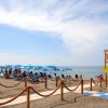 Spiaggia sabbiosa con ombrelloni blu e bagnanti, vista torretta di legno.