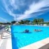 Piscina all'aperto con persone su materassini gonfiabili e cielo parzialmente nuvoloso.