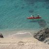 Spiaggia sabbiosa con mare cristallino. Due persone in kayak rosso e una coppia seduta.