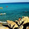 Spiaggia rocciosa con mare cristallino e persone che nuotano.