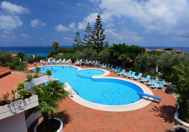 Piscina all'aperto con lettini blu e vista mare.