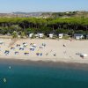 Spiaggia con ombrelloni e sdraio, pineta sullo sfondo, mare calmo.