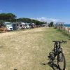 Un'area di campeggio vista mare con camper e bici sul prato.