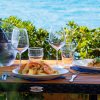 Tavolo con piatti di cibo e bottiglia di vino davanti al mare.