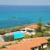 Vista su un villaggio turistico con piscina, alberi e mare cristallino.