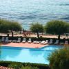 Piscina azzurra vista dall'alto, vicino al mare con sdraio bianche e alberi.