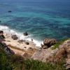 Una spiaggia con sabbia e scogli, mare blu e persone che passeggiano.