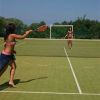 Due persone giocano a tennis su un campo all'aperto sotto un cielo blu.