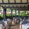Tavoli apparecchiati sotto una veranda all'aperto, circondati da palme e vegetazione.