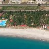 Spiaggia e complesso turistico con piscina e campi sportivi circondati da alberi.
