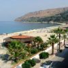 Spiaggia con palme, mare calmo e colline sullo sfondo.