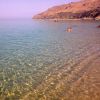 Spiaggia con acqua cristallina e persone che nuotano, colline sullo sfondo.