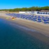 Una spiaggia con sedie a sdraio e ombrelloni blu, vicino al mare con palme sullo sfondo.